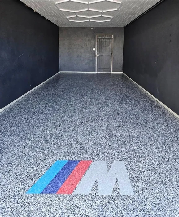 Garage intérieur vide avec sol en résine époxy granuleuse grise, logo BMW coloré intégré au revêtement