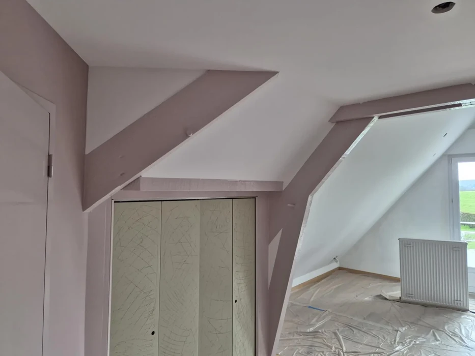 Intérieur de combles aménagés en cours de finition avec charpente apparente peinte
