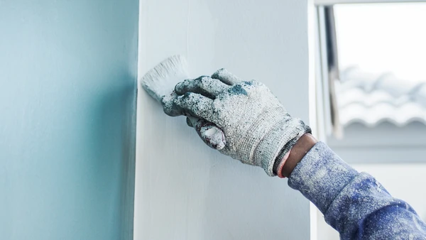 Un ouvrier peint les murs de la maison avec un apprêt à l'aide d'un rouleau de peinture