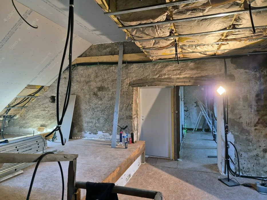 Chantier de rénovation intérieure avec murs en pierre apparente, poutrelles bois au plafond et cloisons en cours d'installation