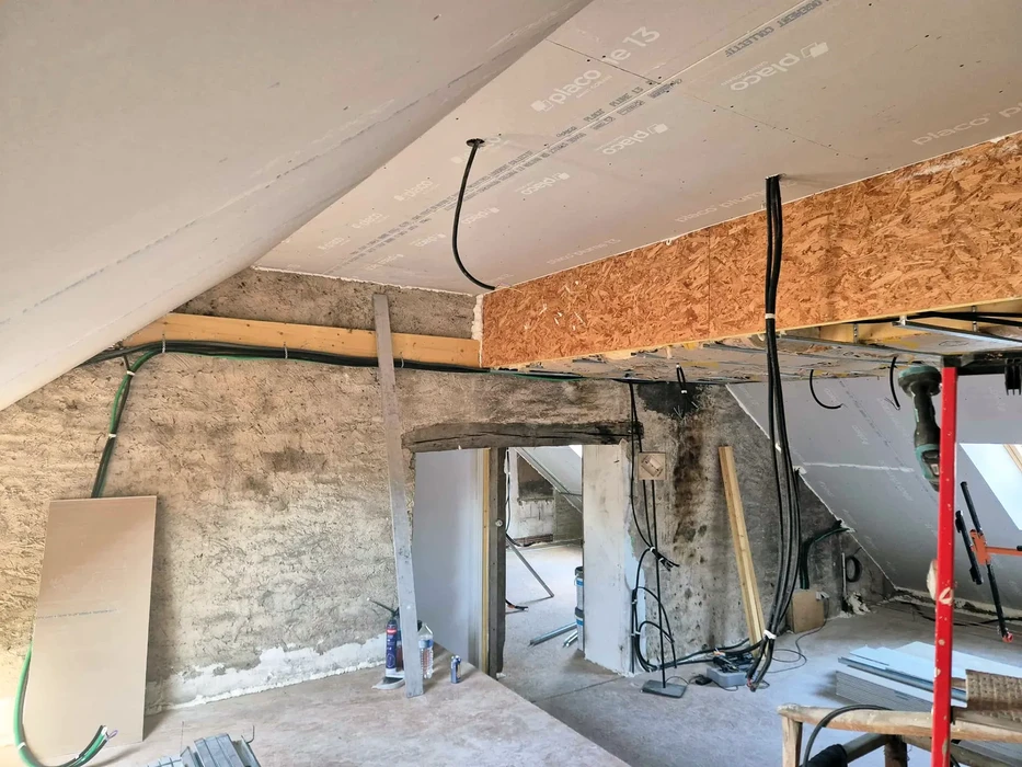 Chantier de rénovation intérieure avec murs en pierre apparente et plafond en cours d'isolation