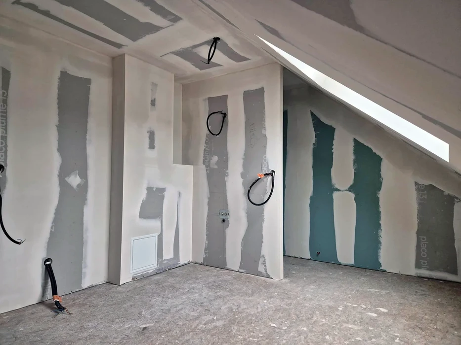 Combles aménagés en cours de finition avec charpente apparente peinte en rose pâle