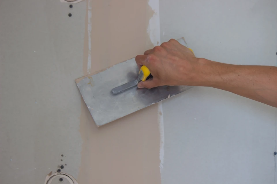 Ouvrier en bleu appliquant un enduit de lissage sur cloison sèche dans salle de bain en rénovation
