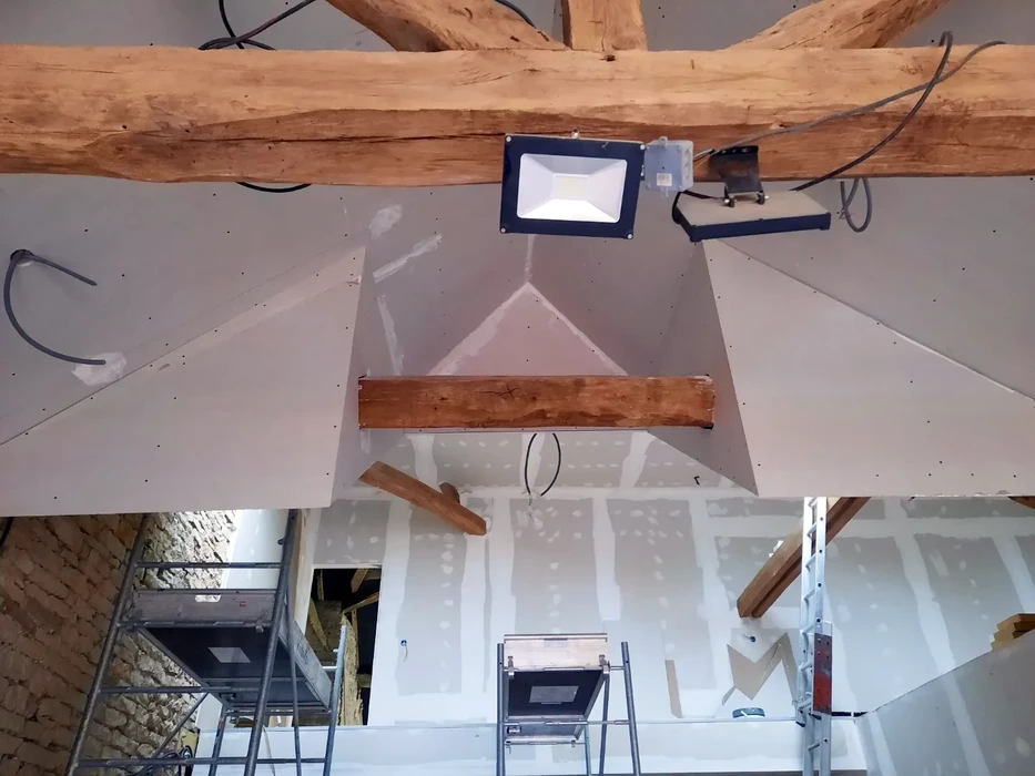 Chantier de rénovation dans combles aménageables avec poutre apparente et lucarne